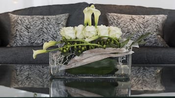 A glass vase with white flowers and green leaves on a reflective surface.