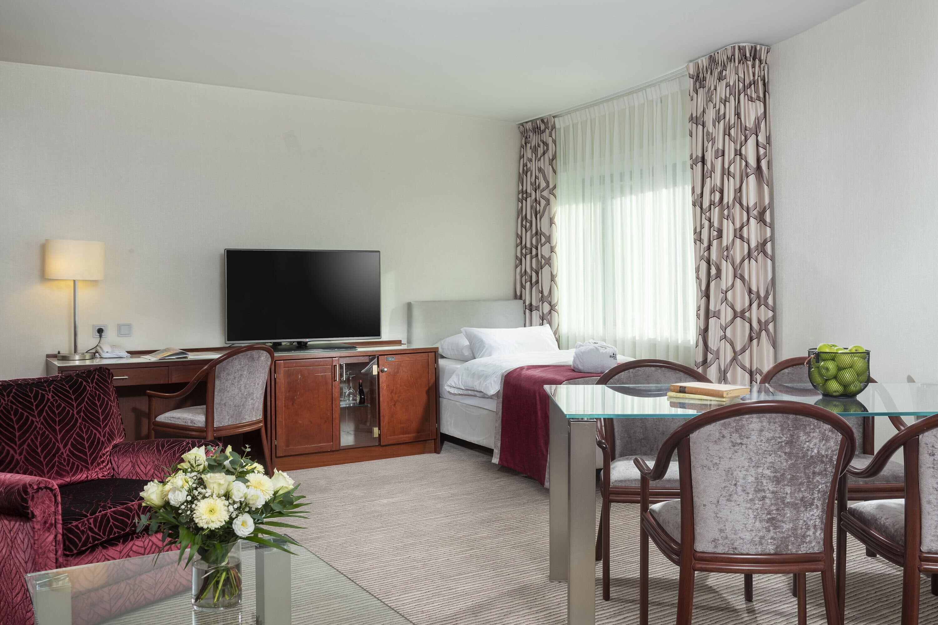 A hotel room with a bed, a TV, a desk, and a dining area with chairs and a table.