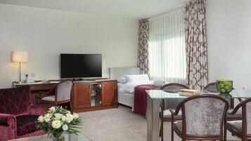 A hotel room with a bed, a TV, a desk, and a dining area with chairs and a table.