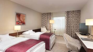 Ein Hotelzimmer mit zwei Betten, einem Schreibtisch, einem Sessel, einem Fernseher und einem Bild an der Wand.