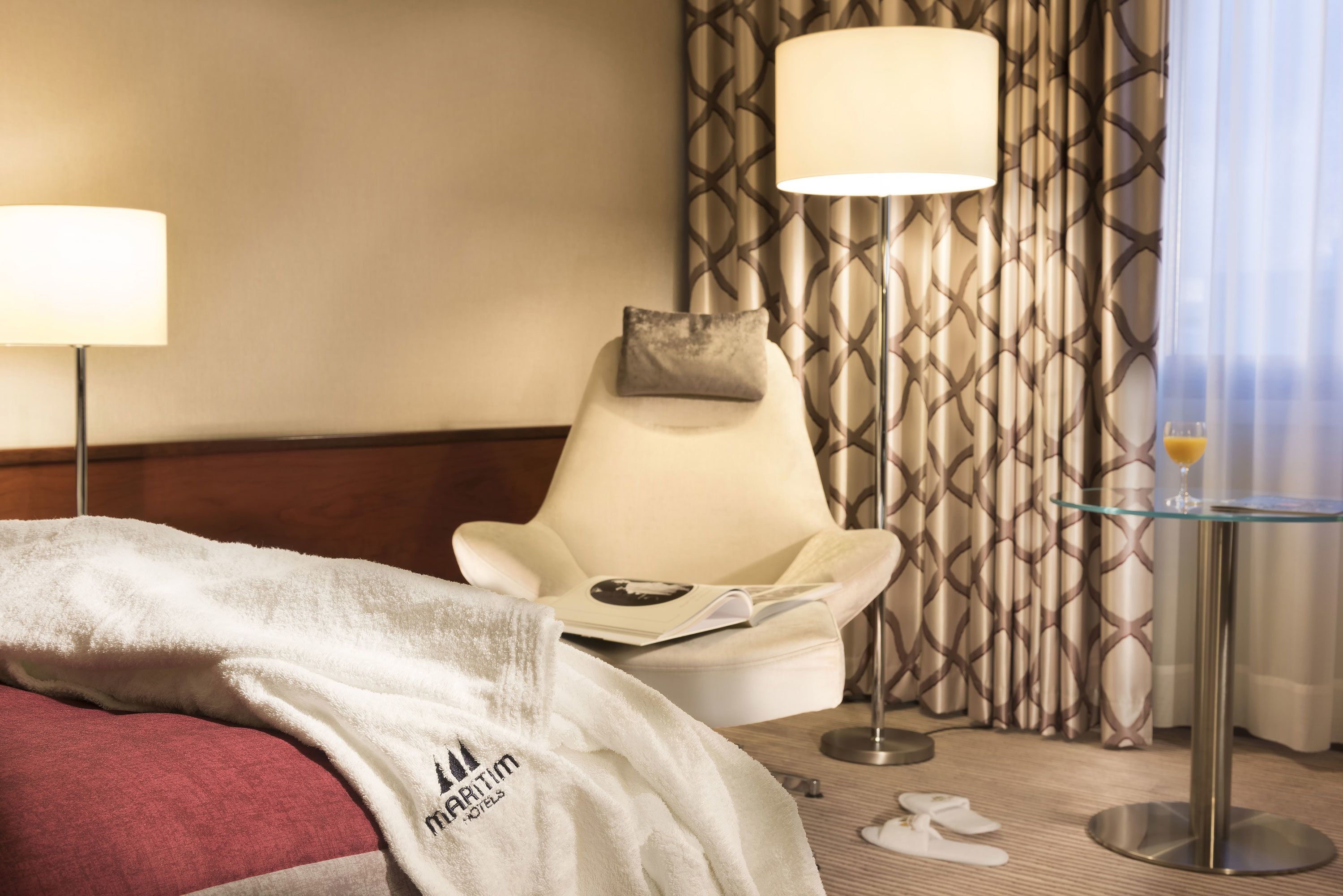 A hotel room with a bed, a chair, a table, and curtains.