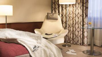 A hotel room with a bed, a chair, a table, and curtains.