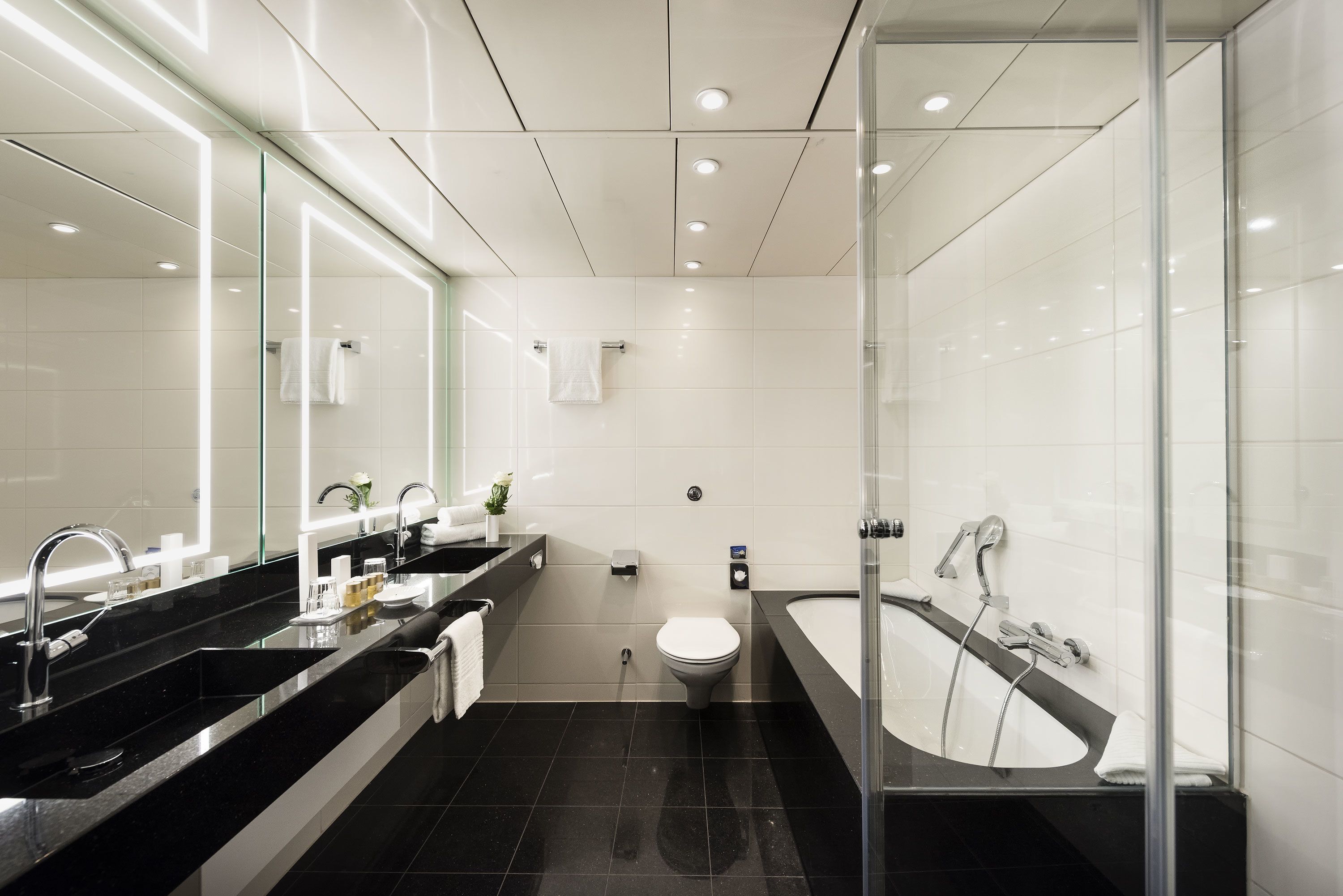 Un baño moderno con lavamanos de superficie negra, inodoro y zona de ducha con mampara de vidrio.
