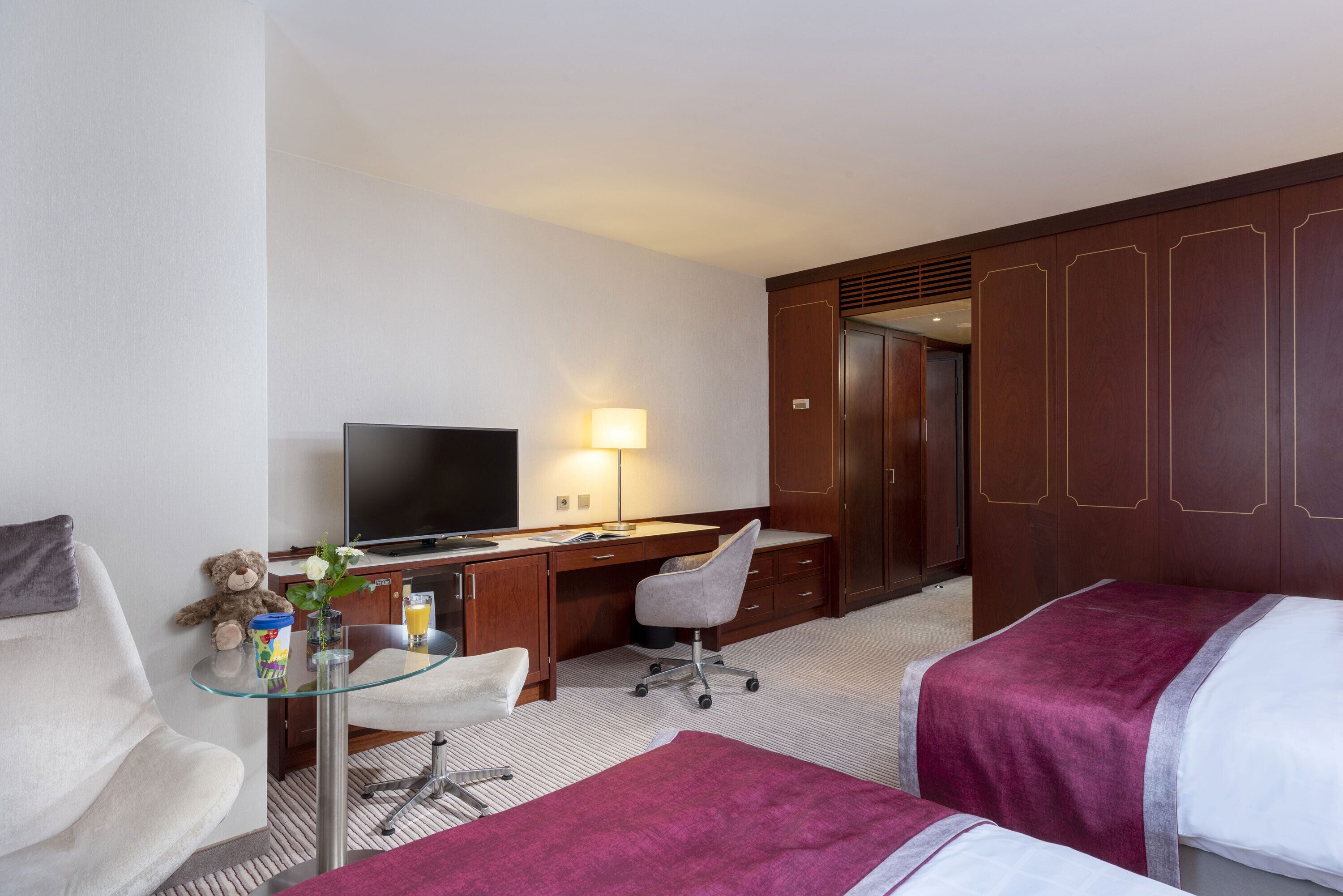 A hotel room with a bed, a desk with a computer, a chair, a television, and a wardrobe.