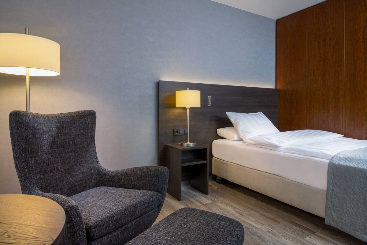 Ein Hotelzimmer mit einem Bett, einem Sessel, einem Nachttisch und einer Lampe.