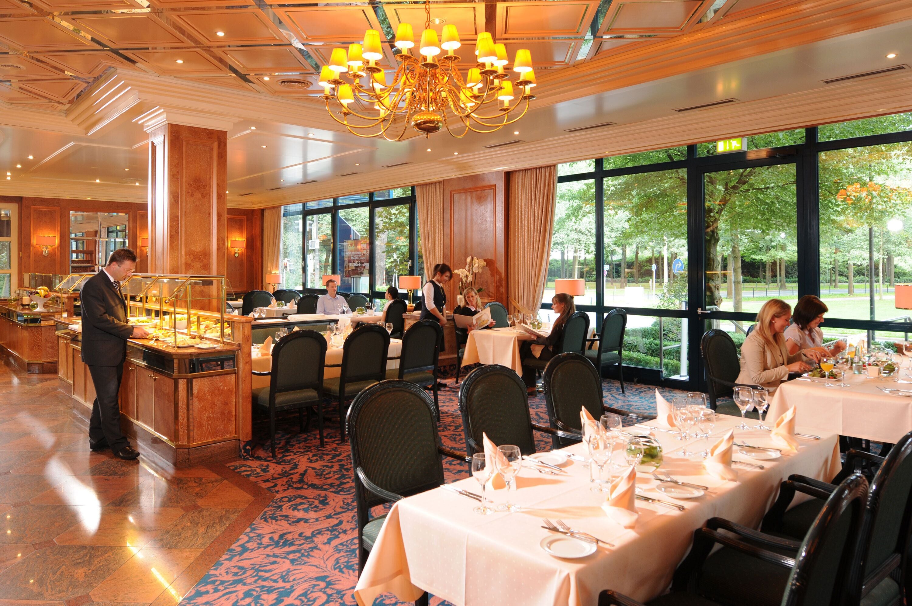 A formal dining area with tables set for guests, a bar area, and large windows offering a view of the outdoors.
