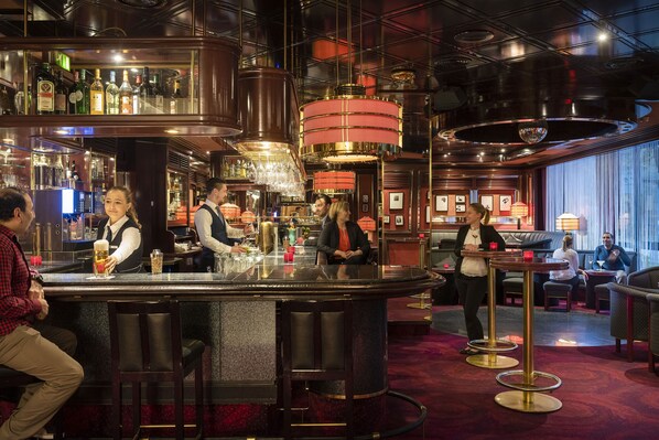 Un espace bar comprenant un comptoir, des tabourets et un coin salon avec des tables et des chaises.