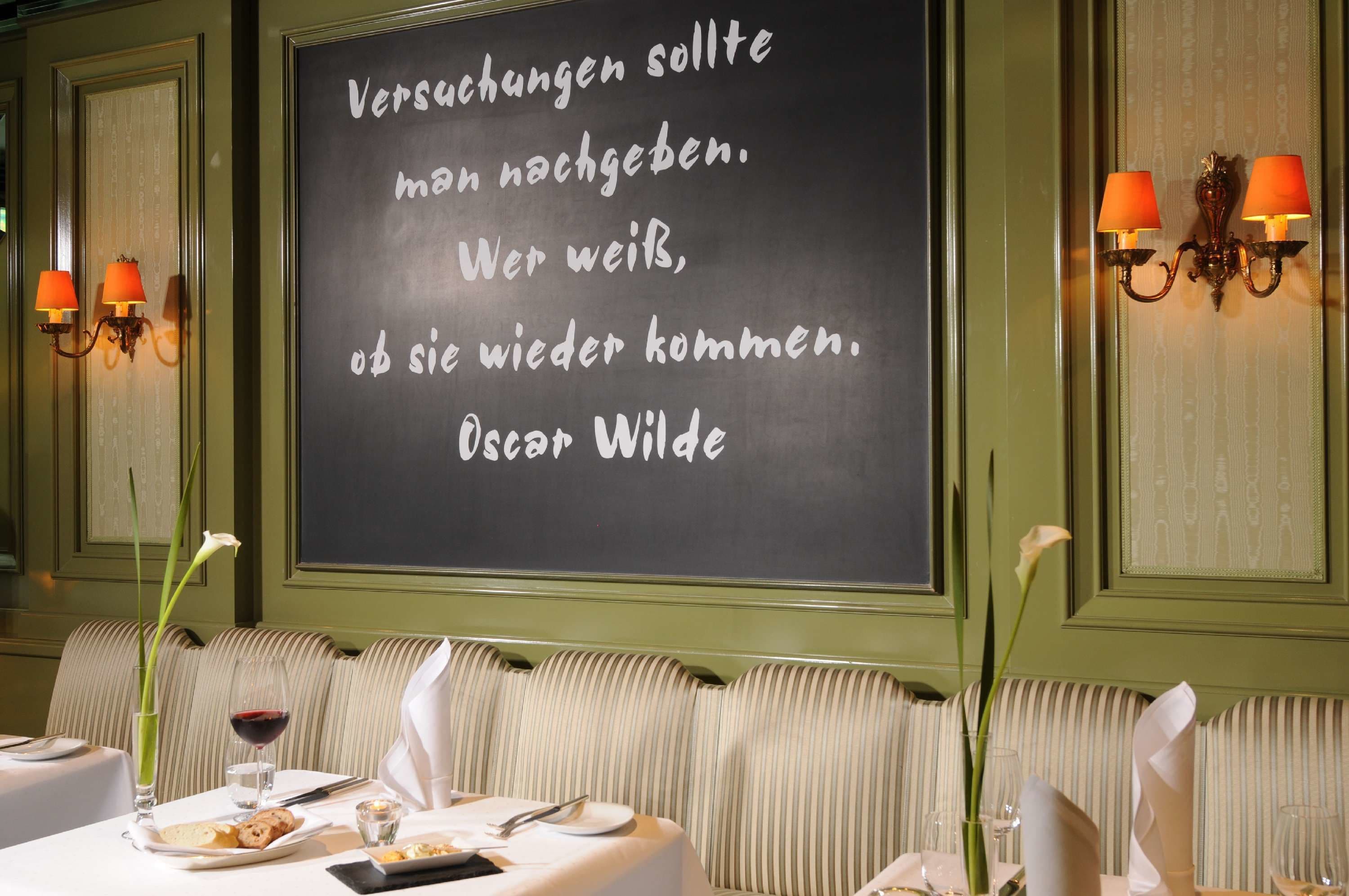 A restaurant interior with a chalkboard displaying a quote, striped upholstered seating, and table settings with wine glasses and plates.