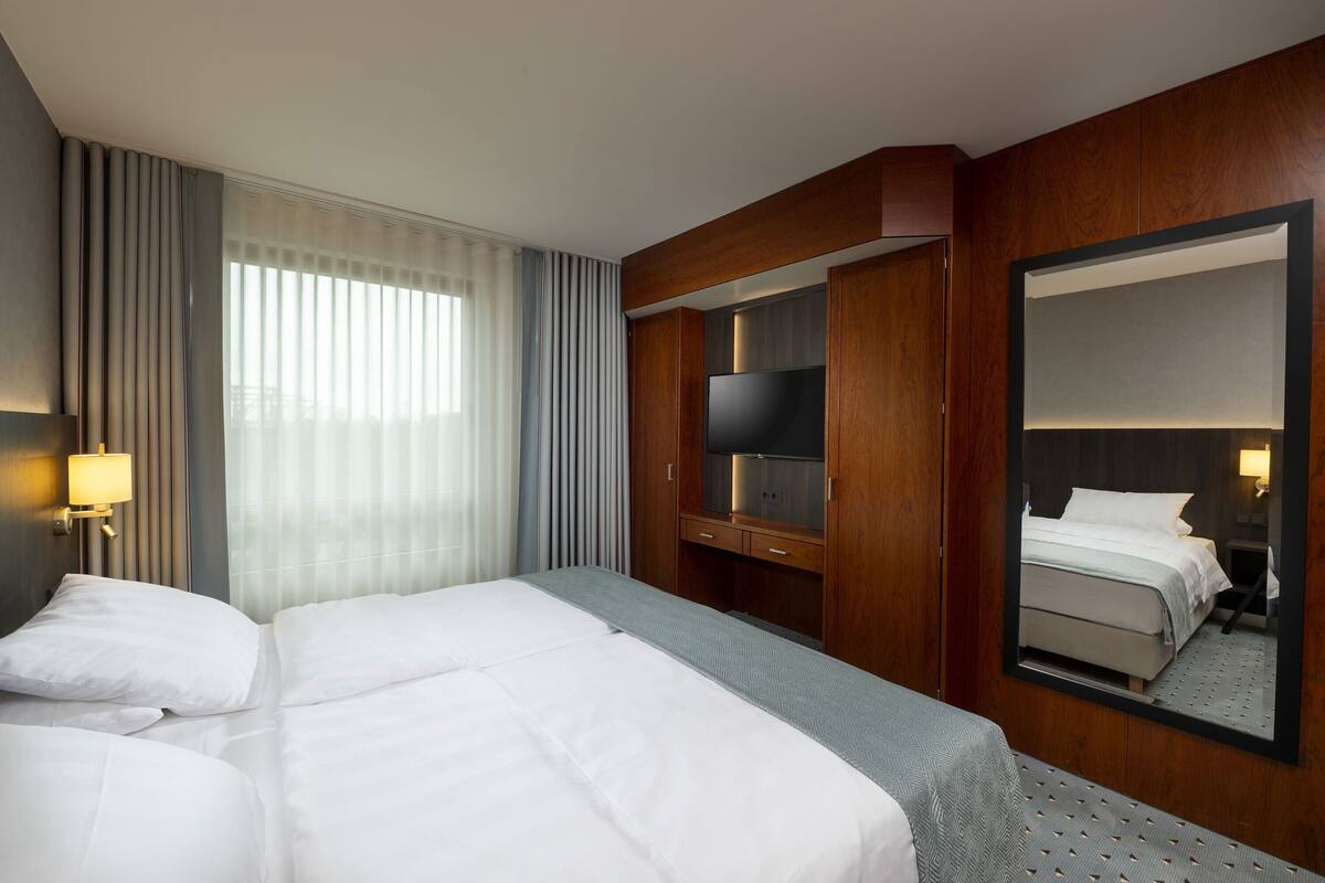 Ein Hotelzimmer mit einem großen Bett, einem Fernseher, einem Spiegel und einem Schreibtisch.