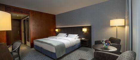 A hotel room with a bed, two bedside tables, a desk, a chair, and a small table with a vase of flowers.
