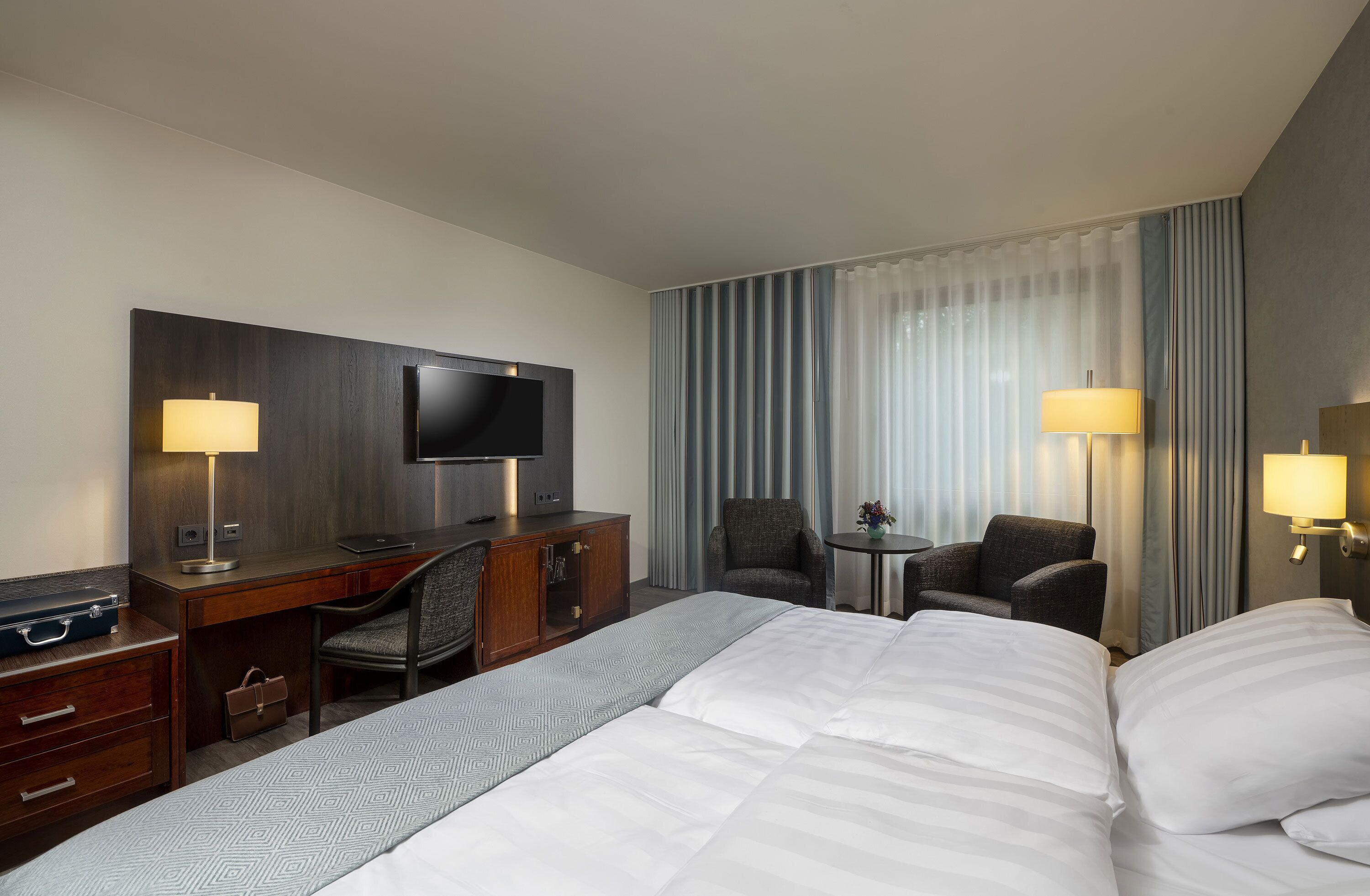 Habitación de hotel con una cama grande, un escritorio con una silla, un televisor y dos lámparas.