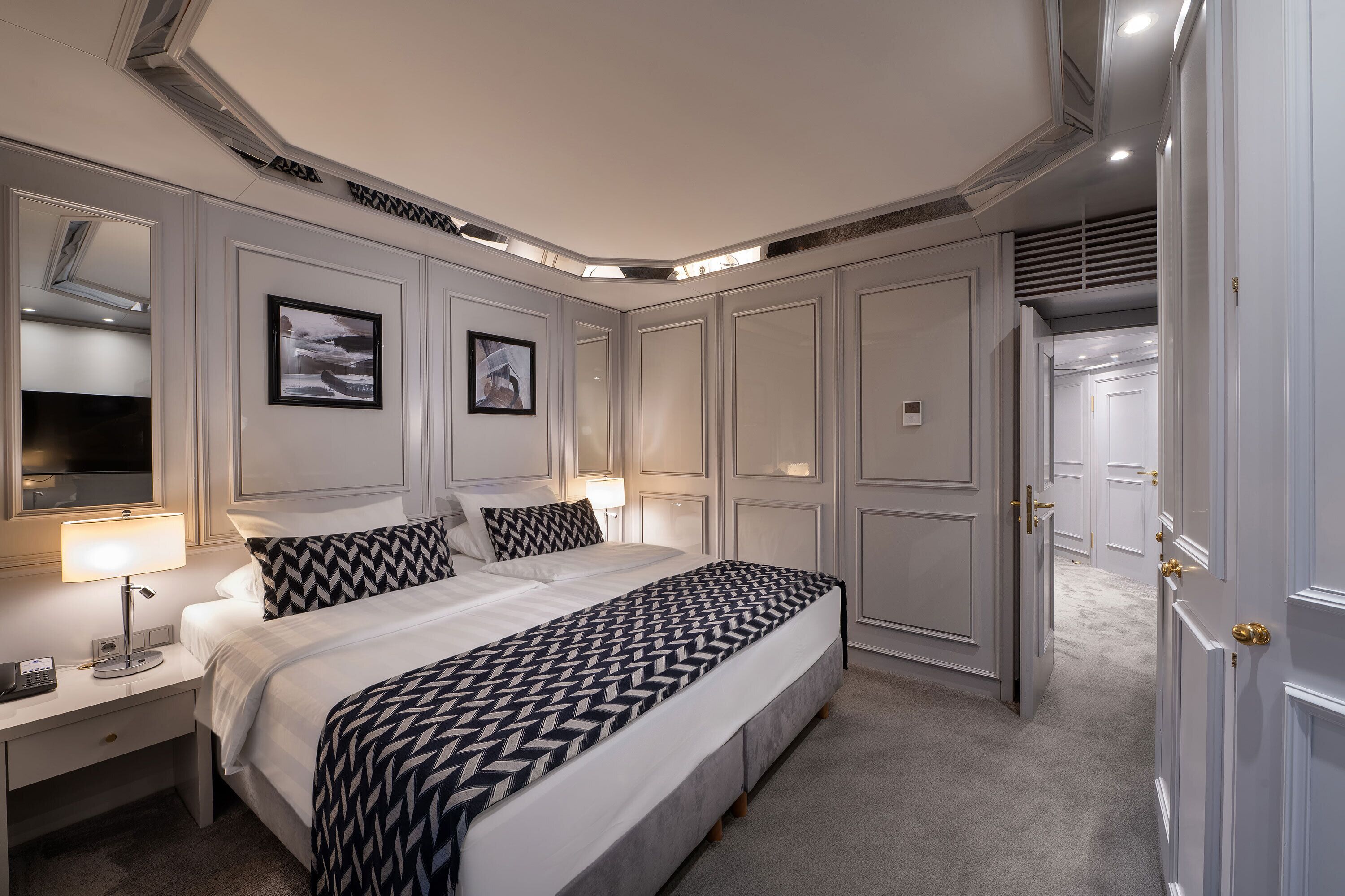 Una habitación de hotel con una cama grande, una mesita de noche con lámpara, un espejo y un armario.