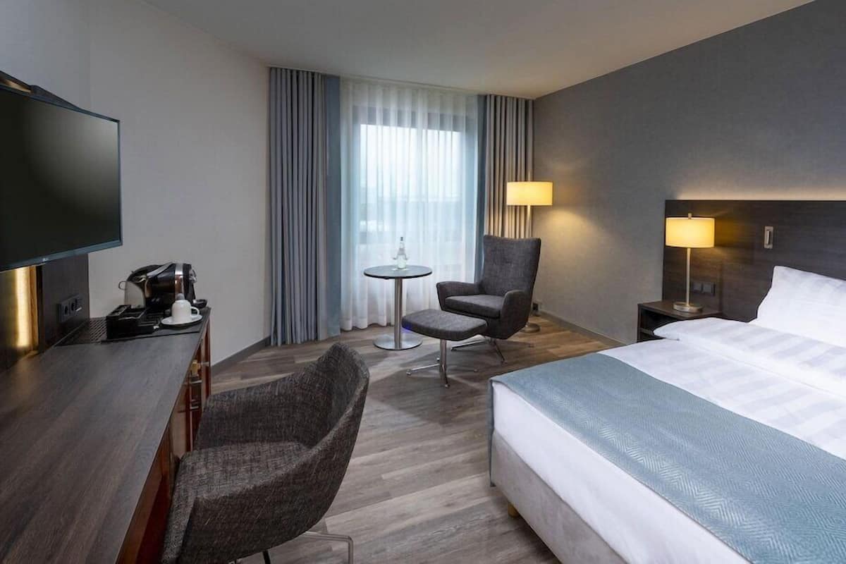 Ein Hotelzimmer mit Bett, Schreibtisch mit Kaffeemaschine, Sessel, kleinem Tisch und Fernseher.