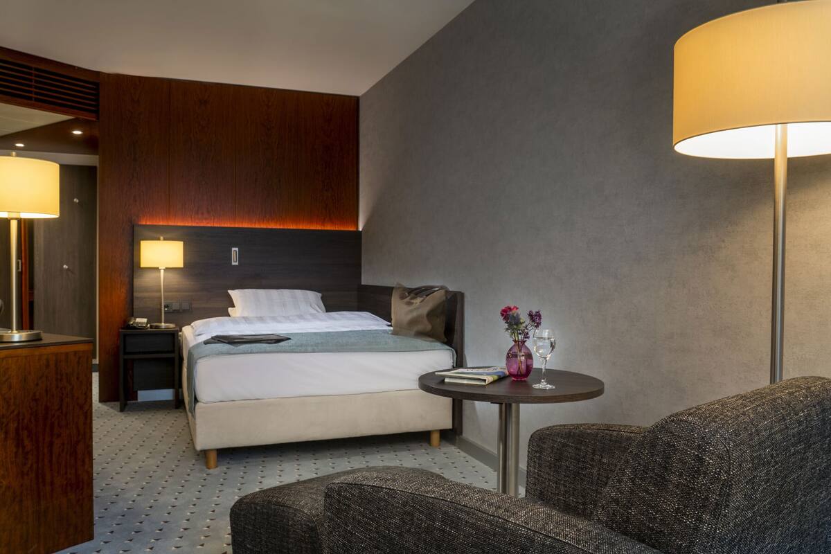 Ein modernes Hotelzimmer mit Bett, Nachttischen, einem Schreibtisch und einem Sessel.
