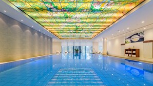 A large indoor swimming pool with a colorful stained glass ceiling and a view of the outdoors through large windows. - Maritim Hotel Bremen (Bremen)