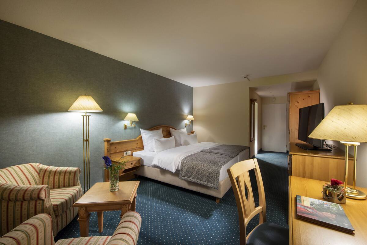 A hotel room with a bed, two bedside tables, a desk, a chair, a sofa, and a television.
