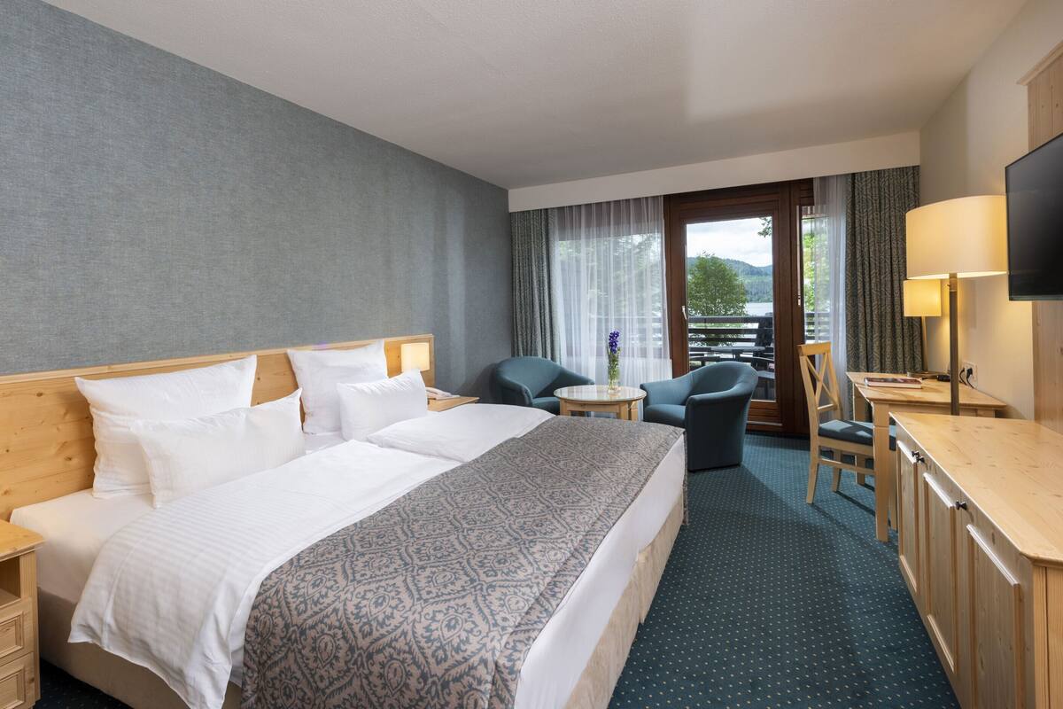 A hotel room with a large bed, a desk, a chair, and a view of the outdoors.