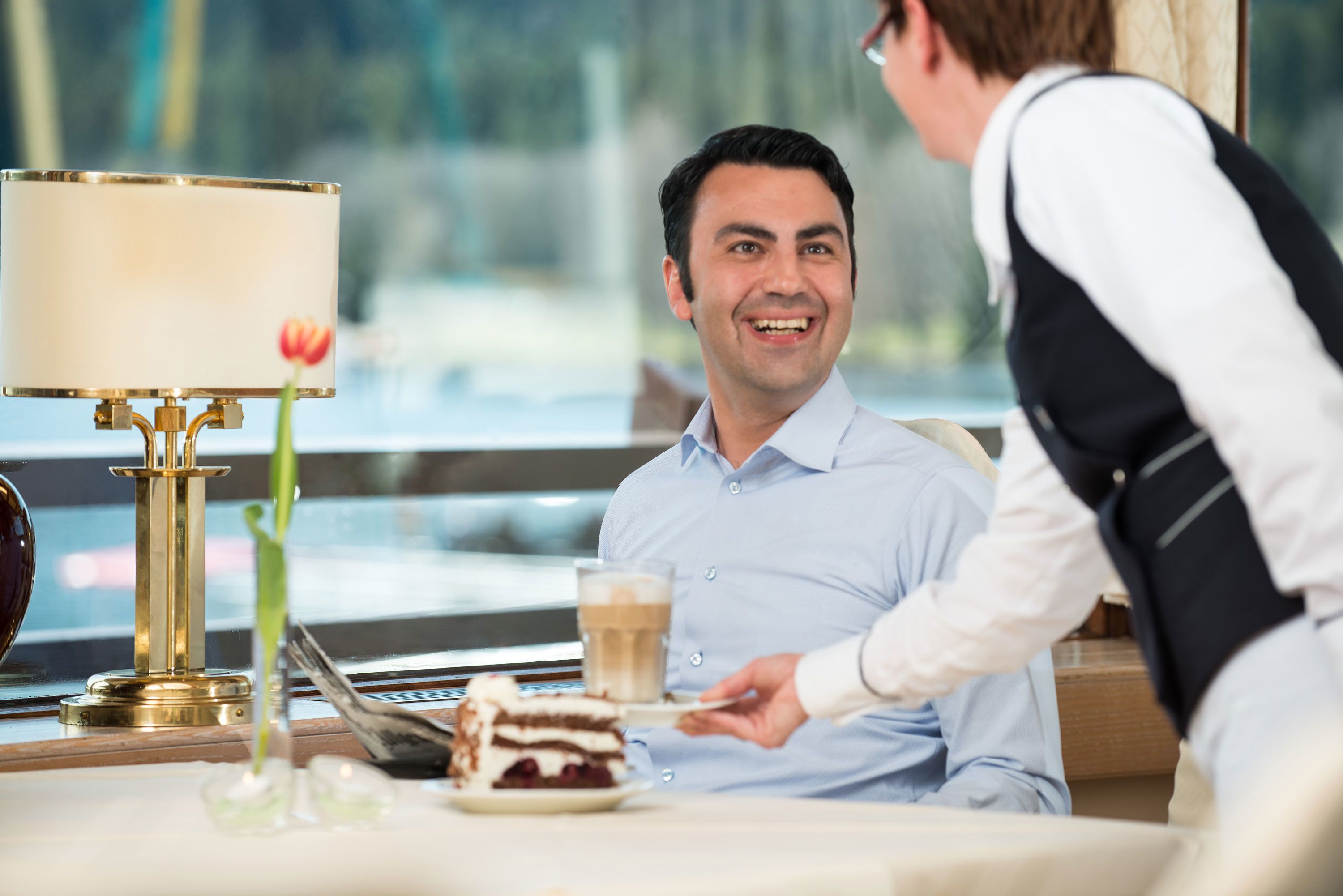 Una persona sentada a una mesa con un pastel y una taza de café.