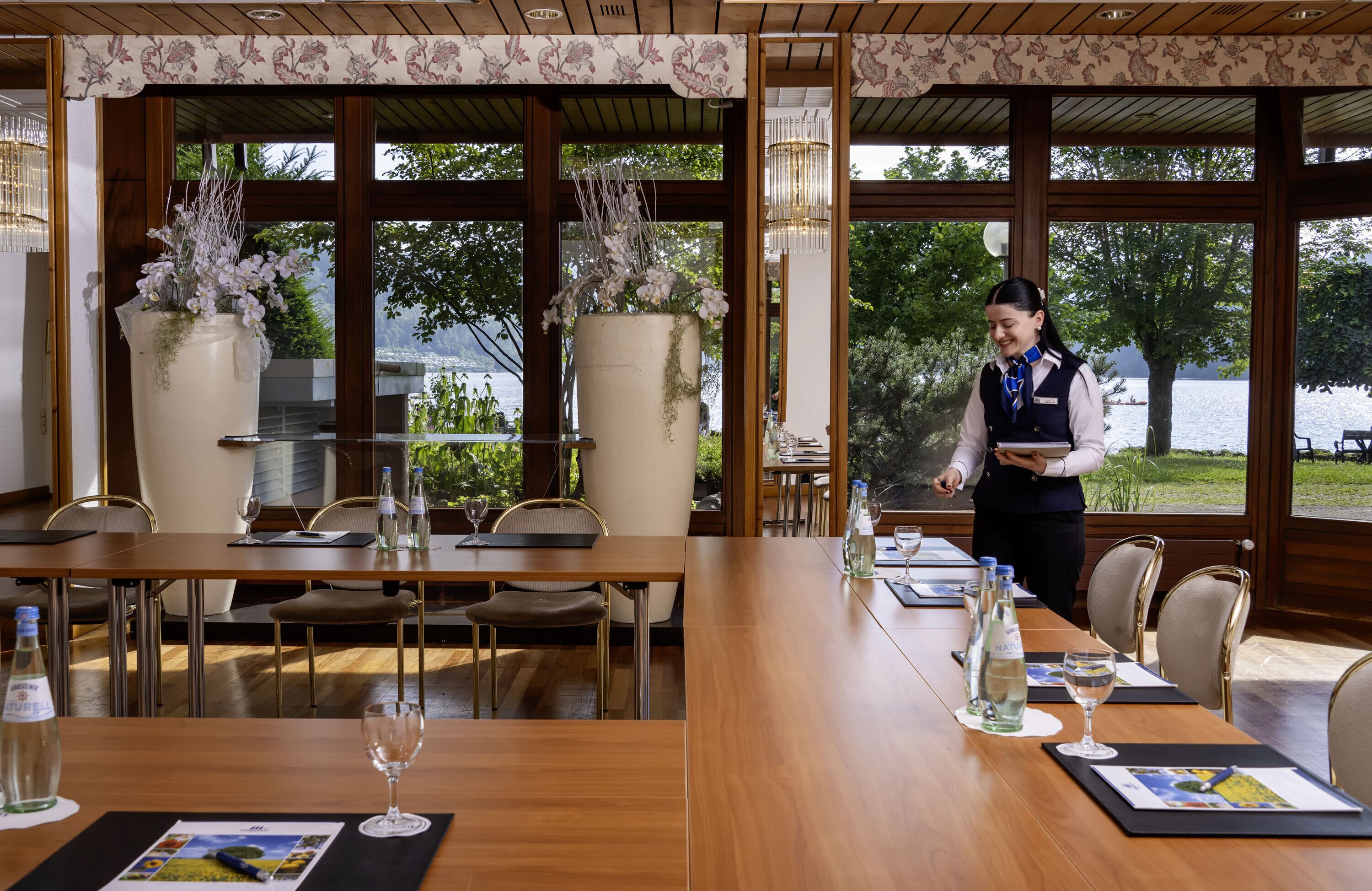 Un restaurante con mesas y sillas de madera, y grandes centros de mesa florales.
