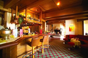 A bar area with wooden furniture, a patterned carpet, and a bar stocked with bottles.