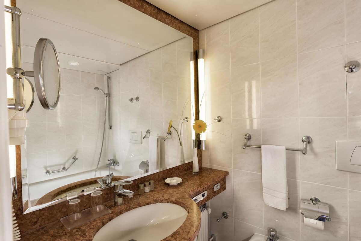 A bathroom with a large mirror, a sink, a towel rack, and a shower.