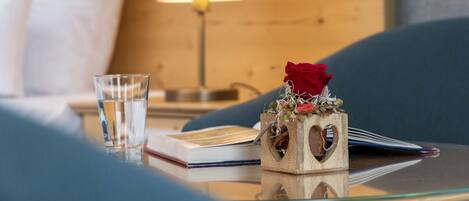 Une chambre d’hôtel bien rangée, avec un lit, une table de chevet sur laquelle se trouve un verre d’eau, un livre et un bloc de bois décoratif orné d’une rose rouge.