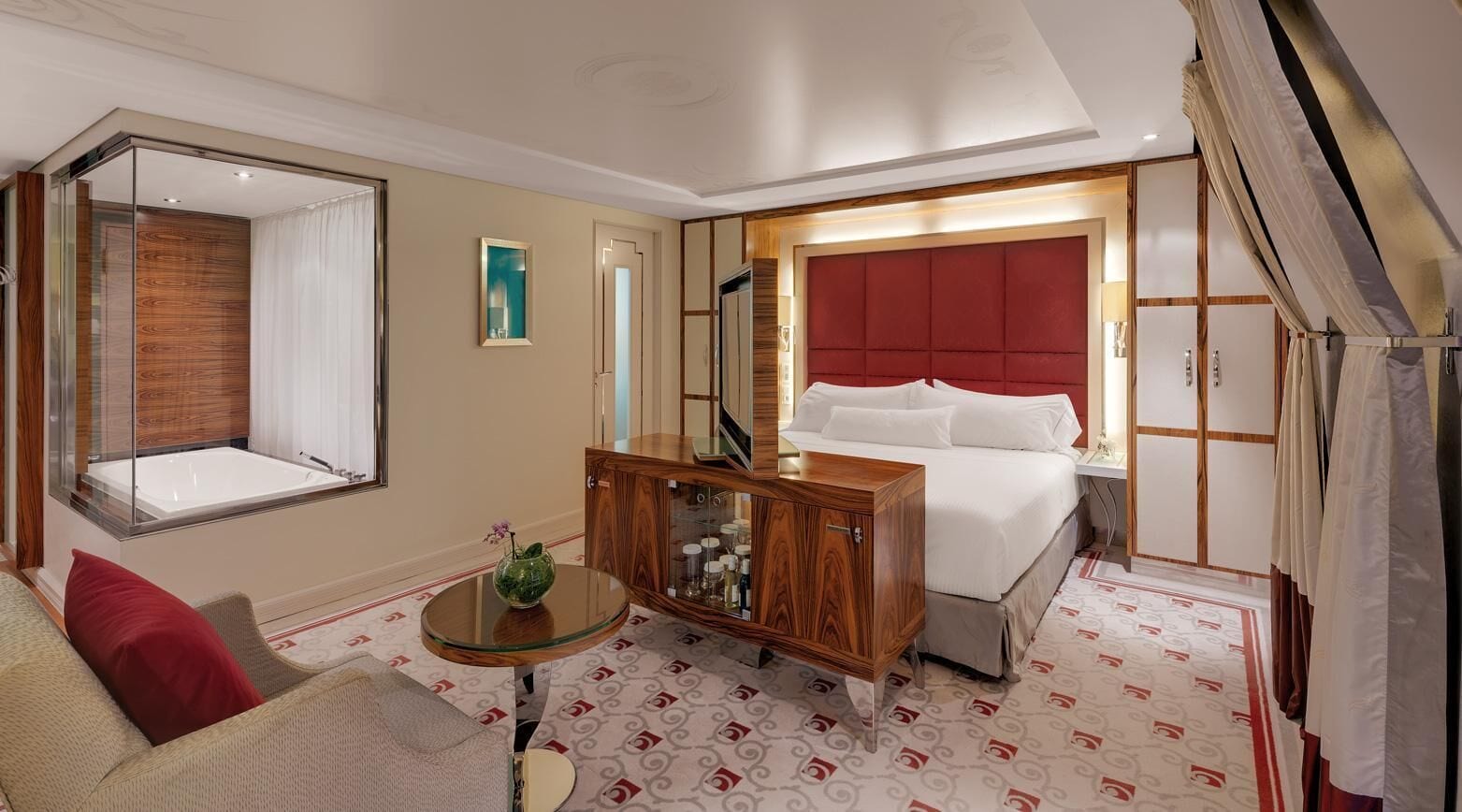 A hotel room with a large bed, a wooden nightstand, a glass coffee table, a sofa, and a large mirror.