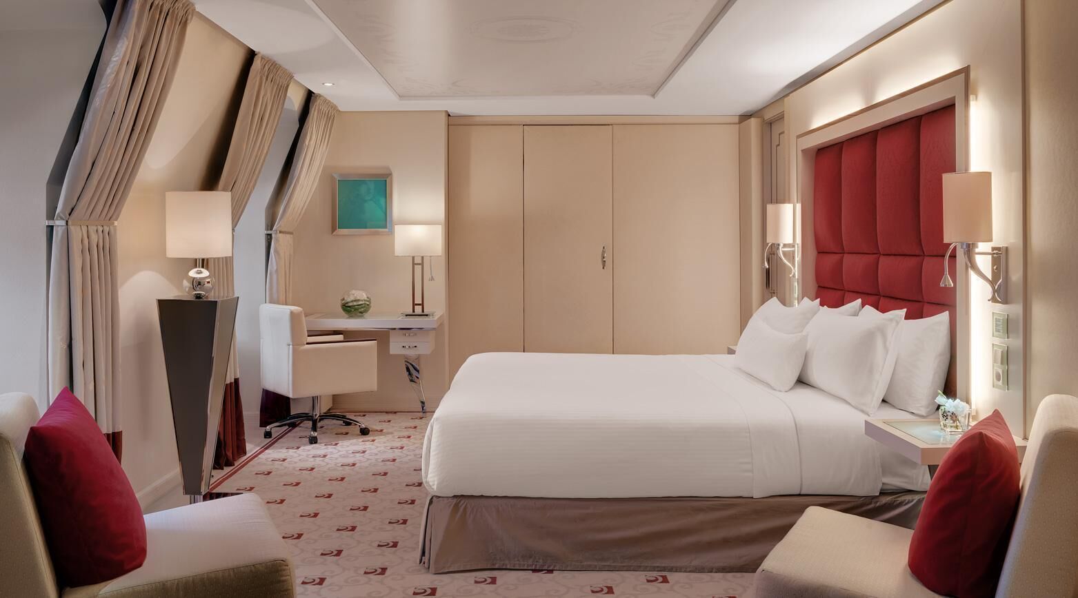A hotel room with a bed, desk, chair, and a large window with curtains.
