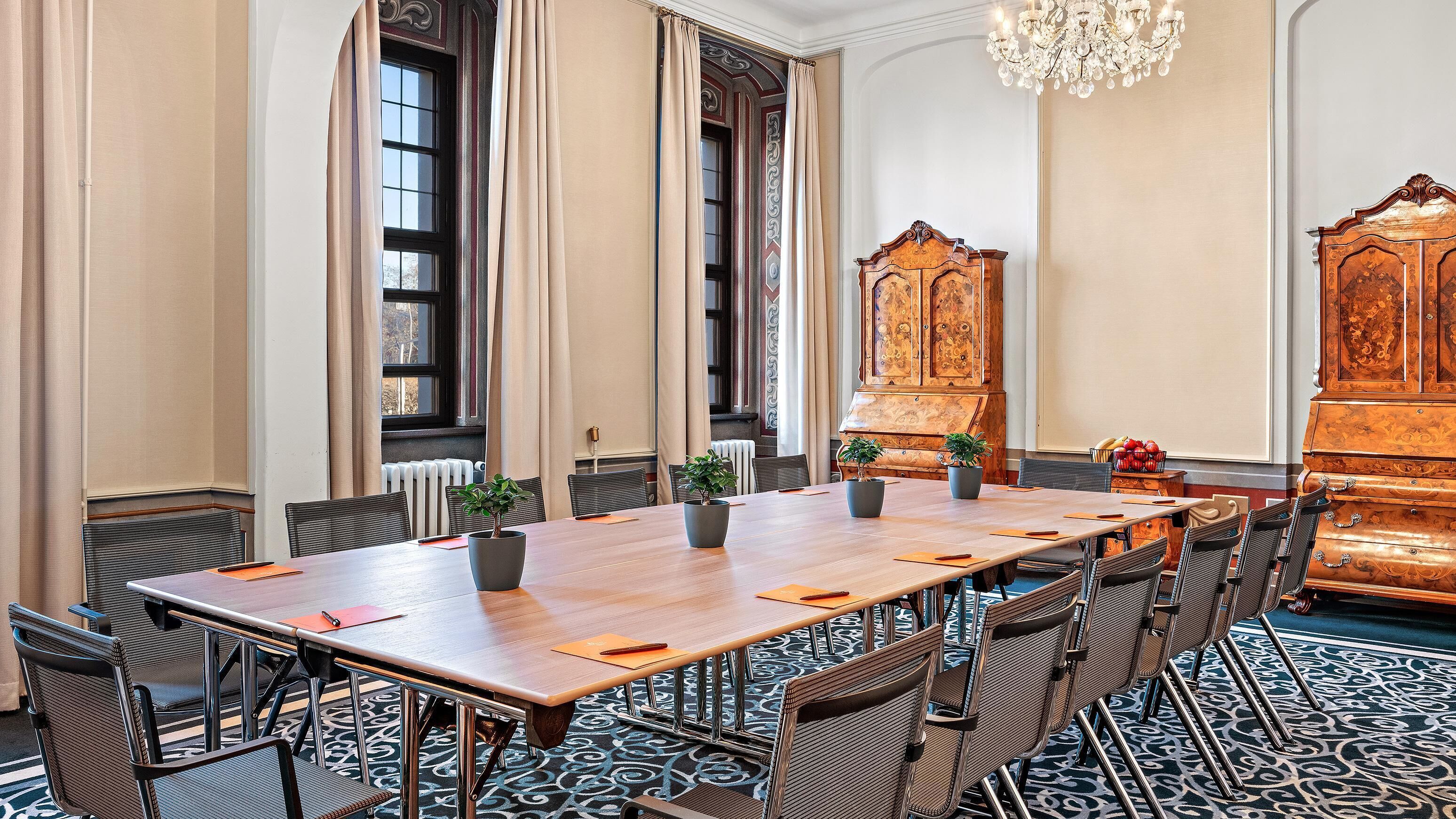 Un salón de conferencias con una larga mesa, sillas, plantas en macetas y un mueble de madera grande.