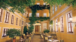Un patio interior con paredes amarillas, varias ventanas y mesas con sillas.