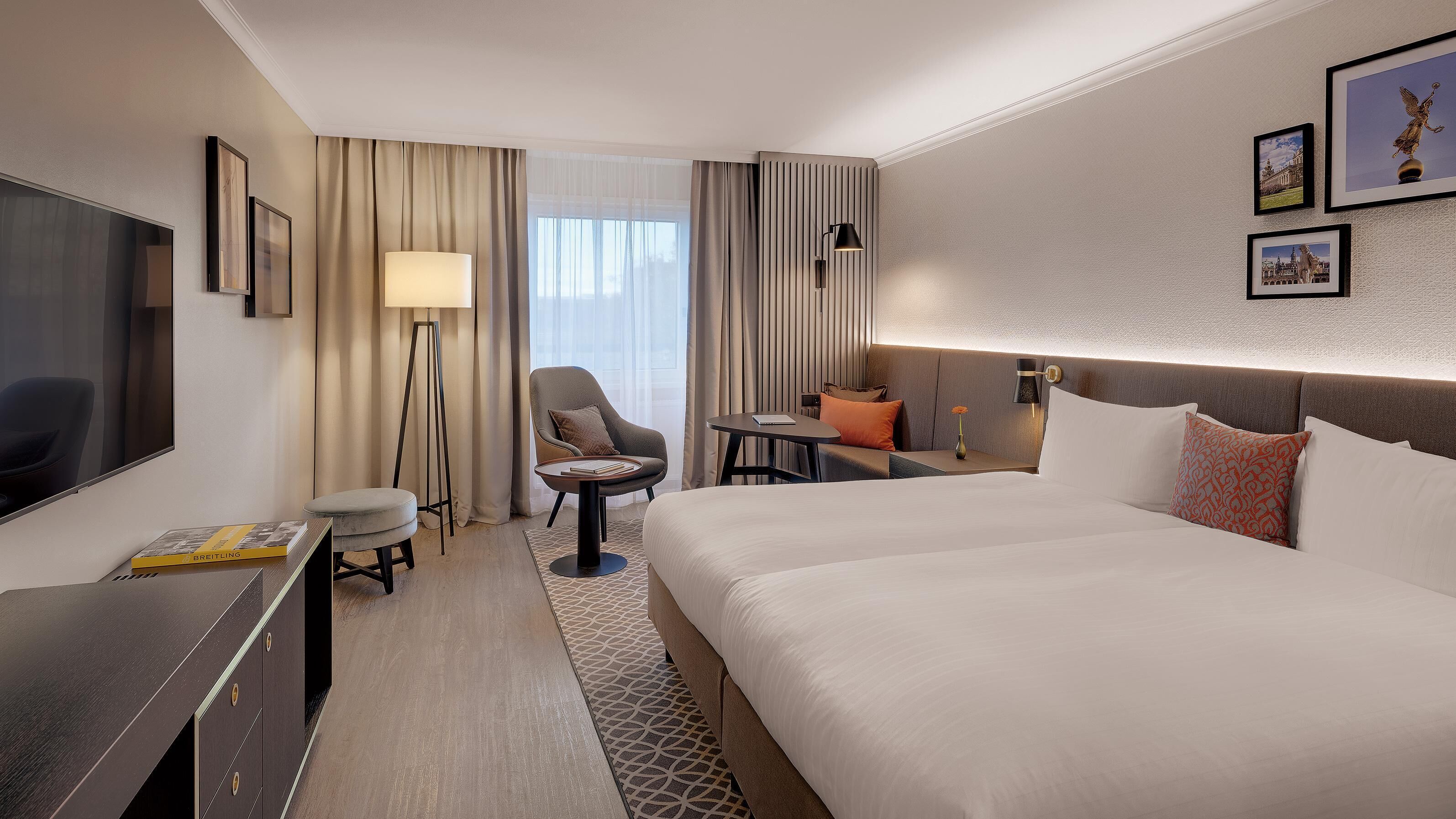 Hotellihuone, jossa on suuri sänky, työpöytä tuolilla, sohva, pieni pöytä lampun kanssa ja televisio.