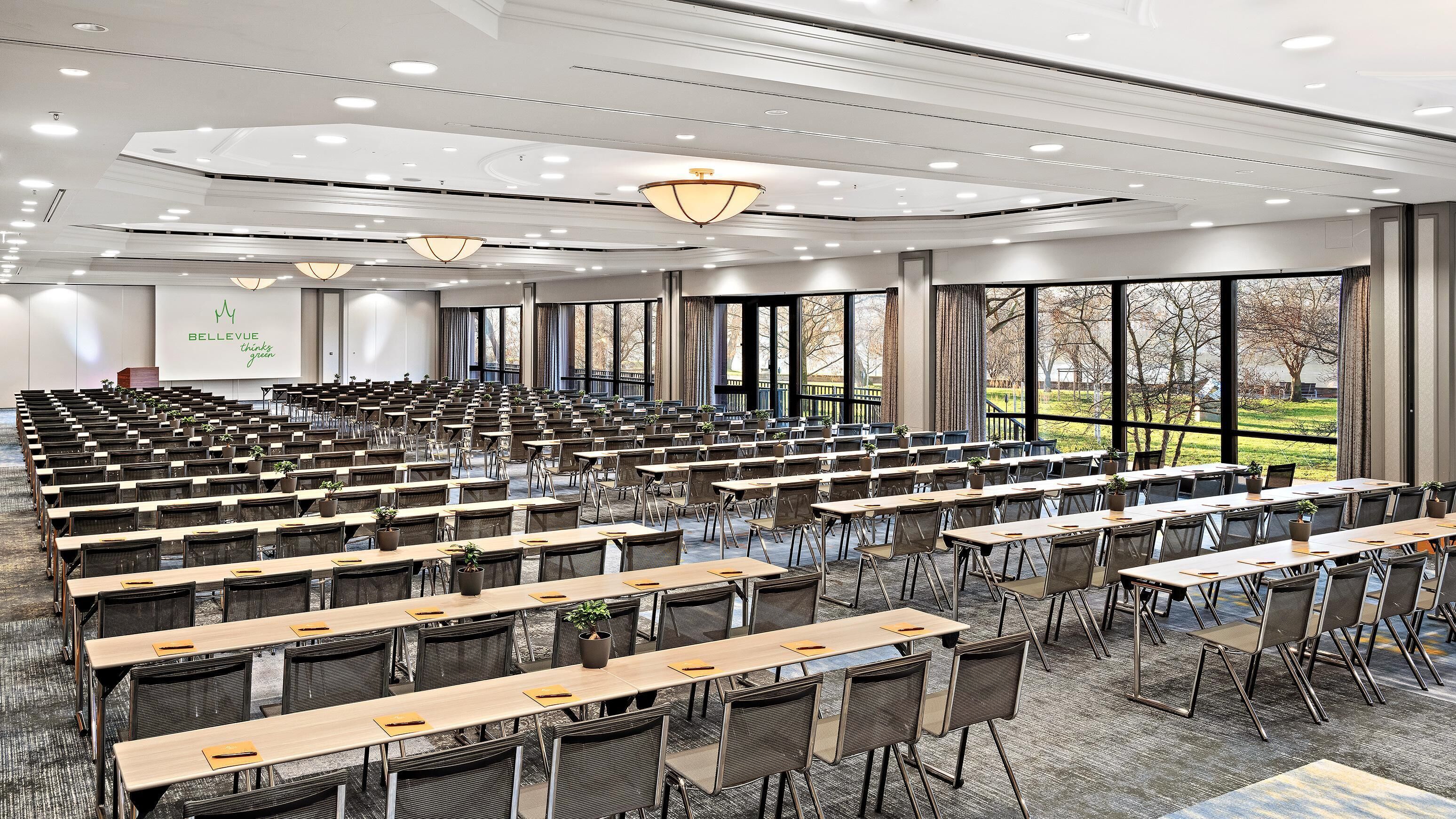 A conference room with rows of tables and chairs, large windows, and a modern ceiling design.