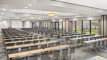 A conference room with rows of tables and chairs, large windows, and a modern ceiling design.