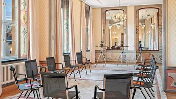 A spacious room with large windows, a chandelier, and multiple chairs arranged for seating.