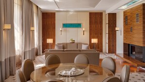 A modern hotel room with a central seating area, a glass dining table with chairs, and a fireplace.