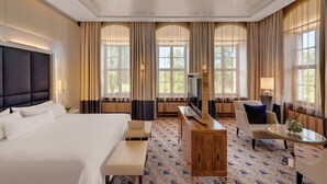 A hotel room with a large bed, a TV, a desk, a chair, and a glass coffee table.