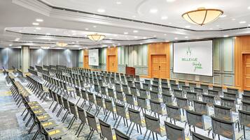 Une salle de conférence avec des rangées de chaises, un grand écran et un pupitre.