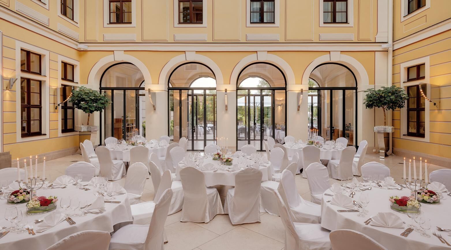 A banquet hall with round tables set for a formal event, featuring white tablecloths, chairs, and floral centerpieces.