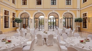 Un salón de banquetes con mesas redondas dispuestas para un evento formal, con manteles blancos, sillas y centros de mesa florales.