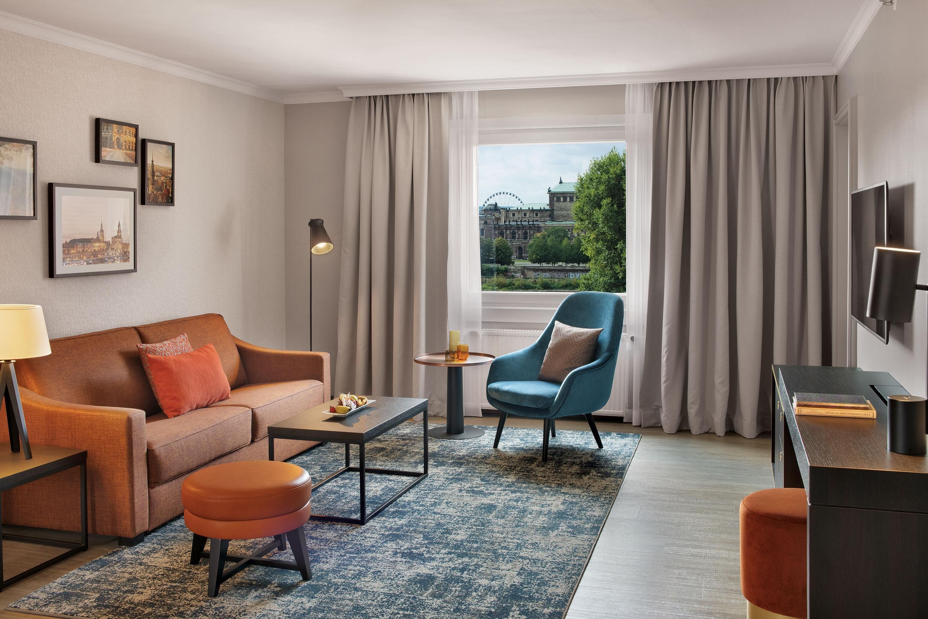 Ein modernes Hotelzimmer mit Sofa, Sessel, Couchtisch und Fernseher.