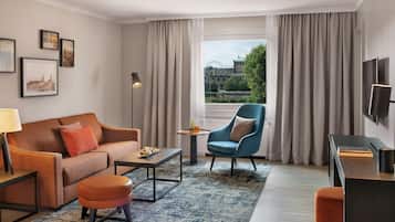 Una habitación de hotel moderna con sofá, sillón, mesa de centro y televisor.