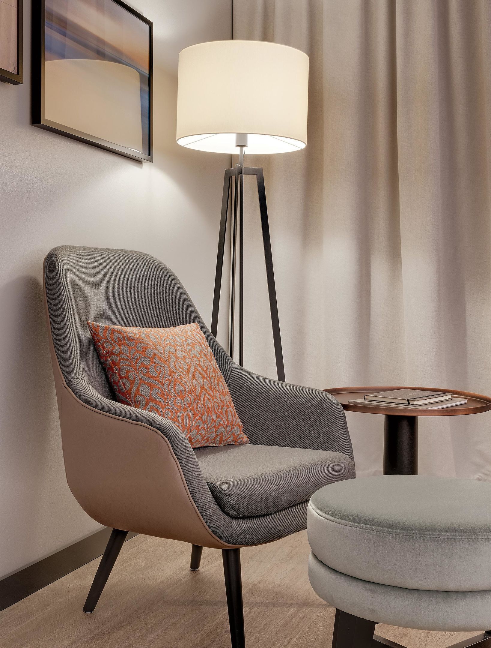 A modern armchair with a patterned cushion, a floor lamp, and a small round table with a book.
