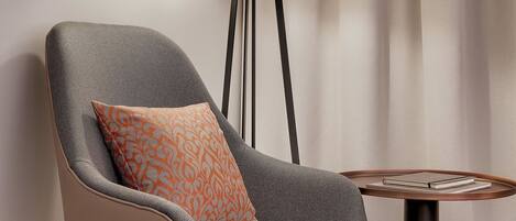 A modern armchair with a patterned cushion, a floor lamp, and a small round table with a book.