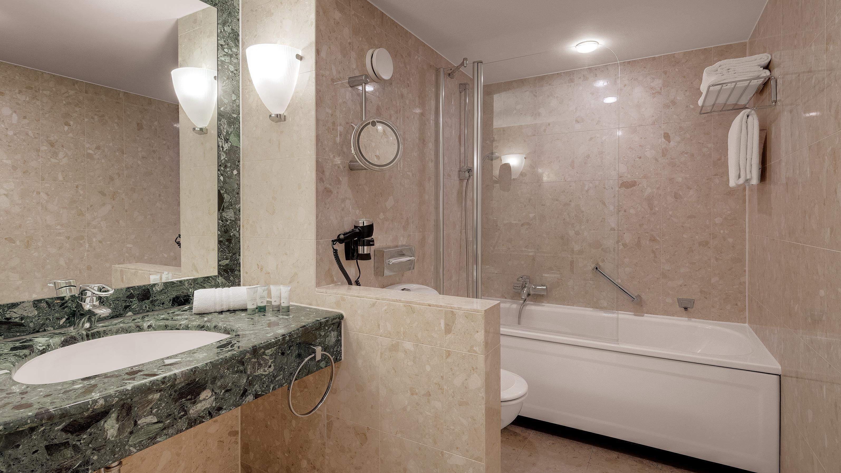 A modern bathroom with a marble sink, a bathtub, and a glass-enclosed shower.