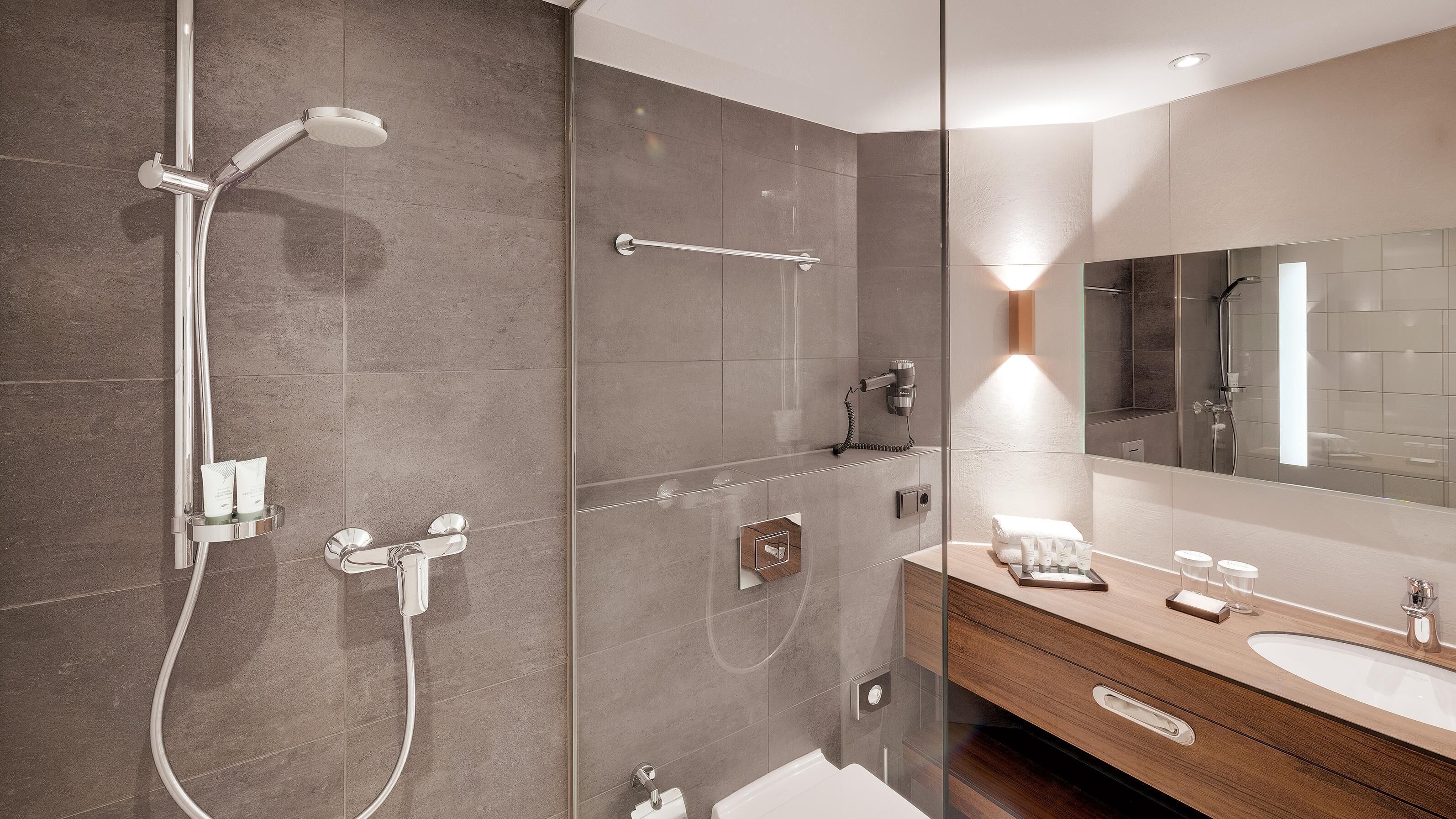 Un baño moderno con cabina de ducha de vidrio, tocador con espejo y perchero.
