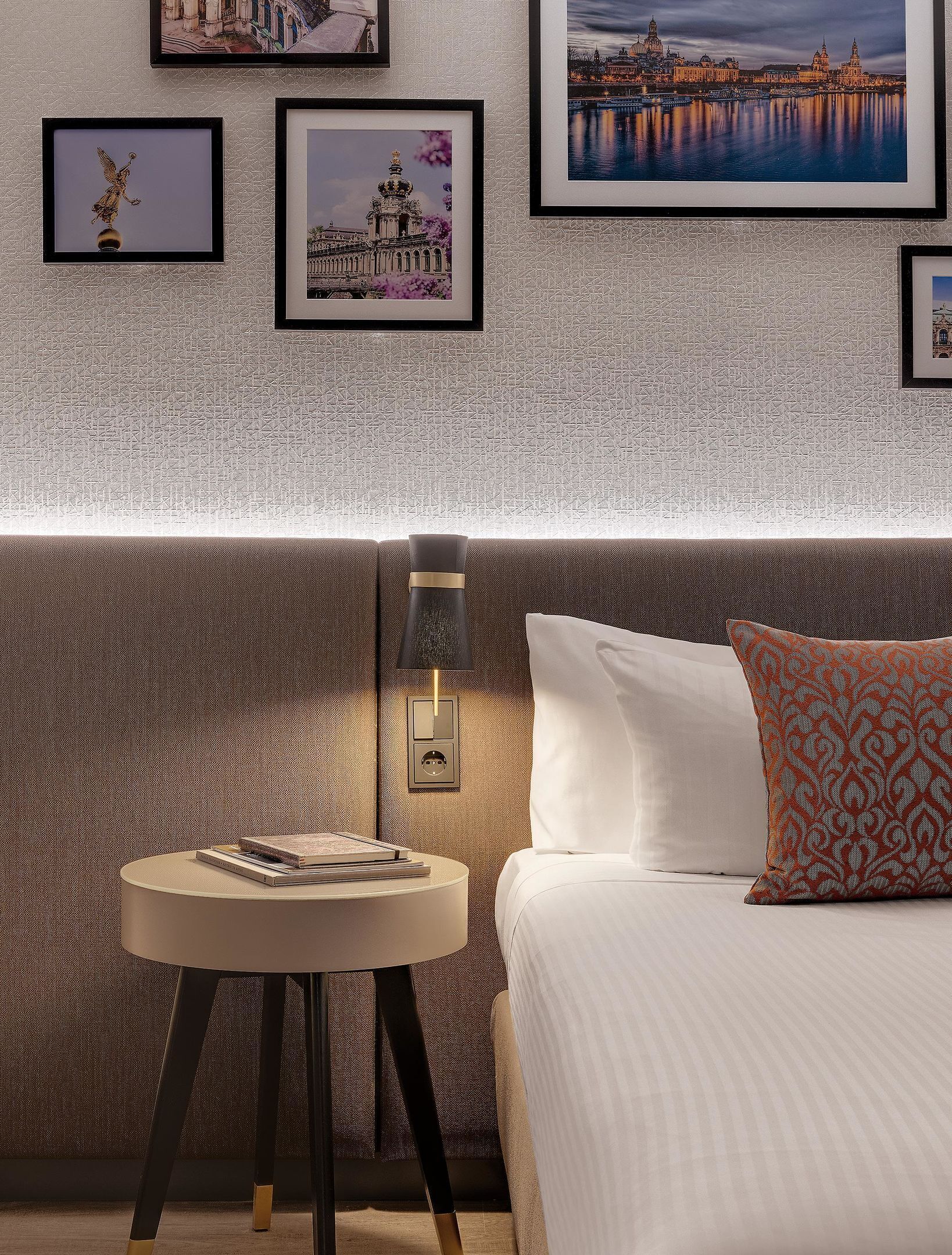Ein Hotelzimmer mit Bett, Nachttisch mit Lampe und gerahmten Bildern an der Wand.