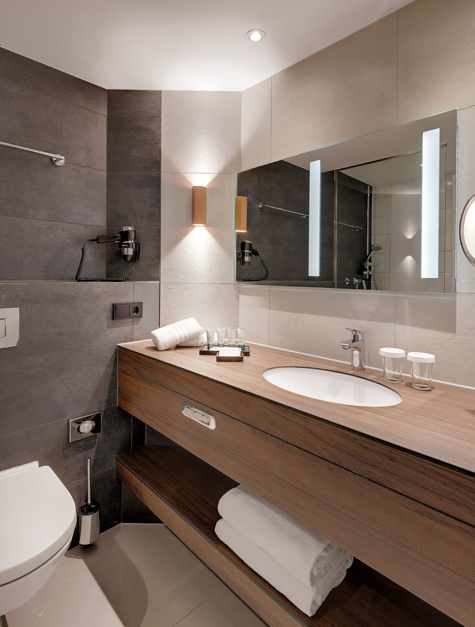 A modern bathroom with a large mirror, two sinks, a hairdryer, and a towel rack.