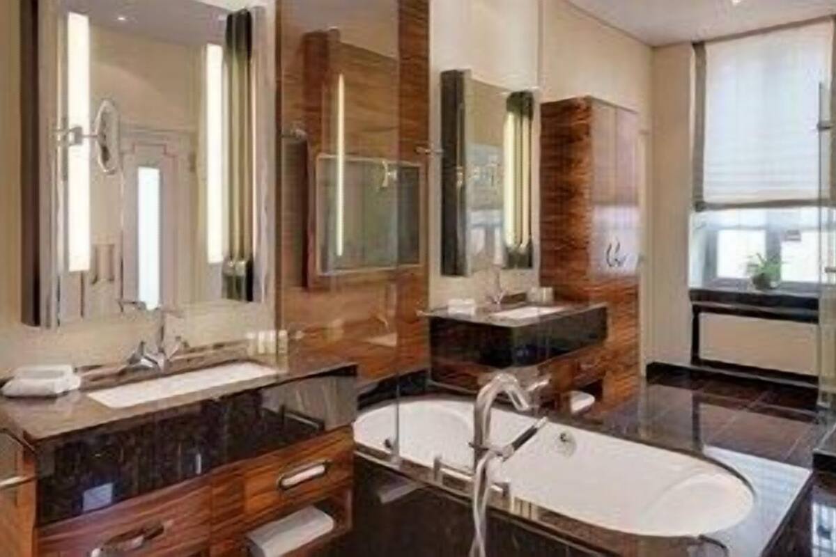 A modern bathroom with a large mirror, two sinks, a bathtub, and a glass shower enclosure.