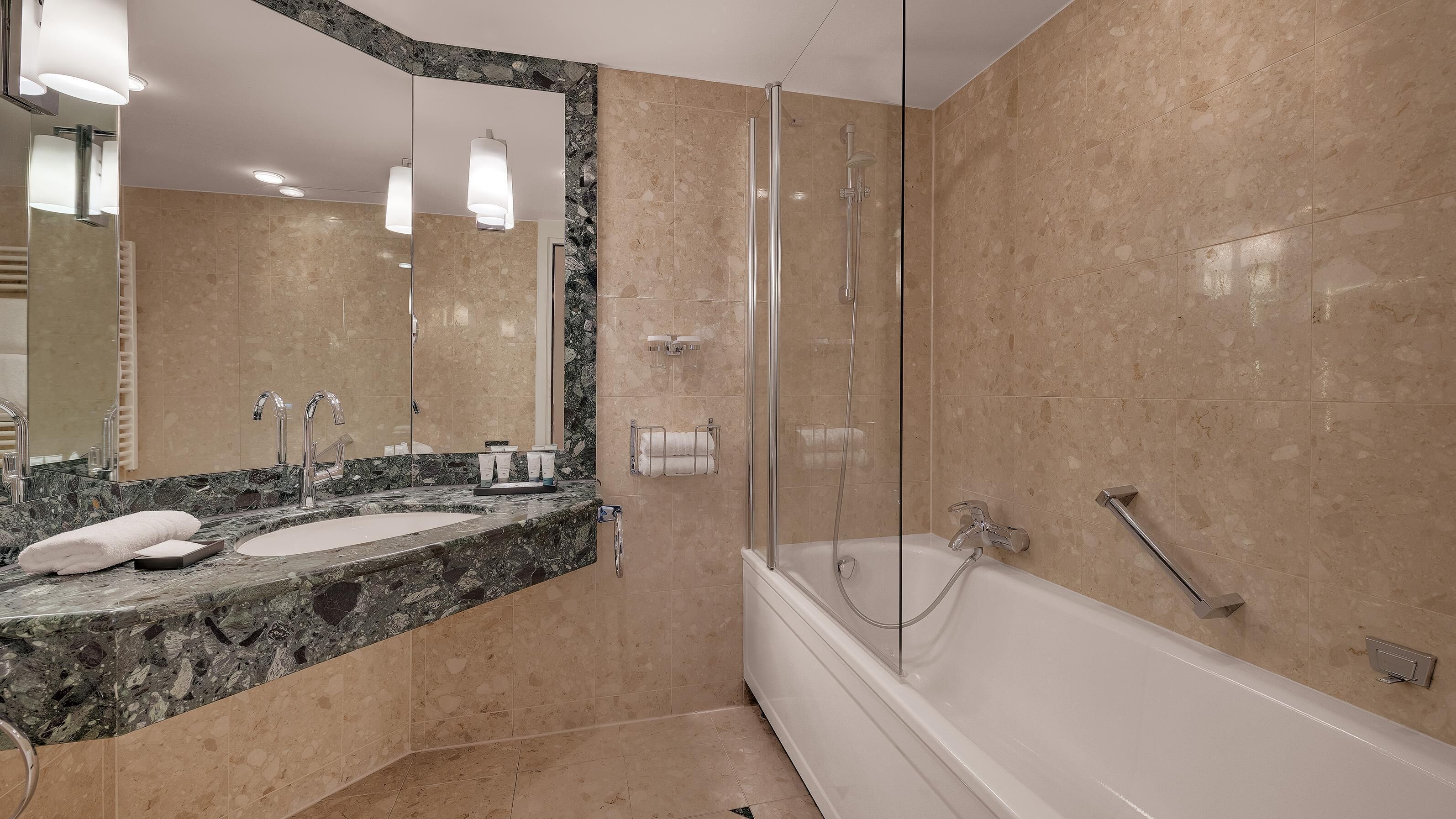 A modern bathroom with a marble vanity, a glass-enclosed shower, and a white bathtub.