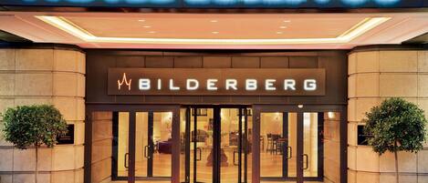 A hotel entrance with a revolving door, a red carpet, and a sign that reads "HOTEL BELLEVUE BILDERBERG".